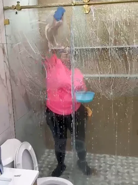 A Milu team member scrubbing shower glass during a deep clean